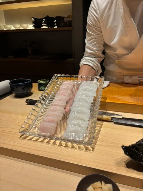 카타오카 아츠시의 유리 쟁반에 두 줄로 담은 회를 보여주는 요리사