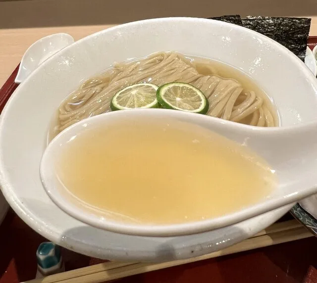 모에요 멘스케의 숟가락에 담긴 맑은 국물과 감귤 슬라이스를 올린 면