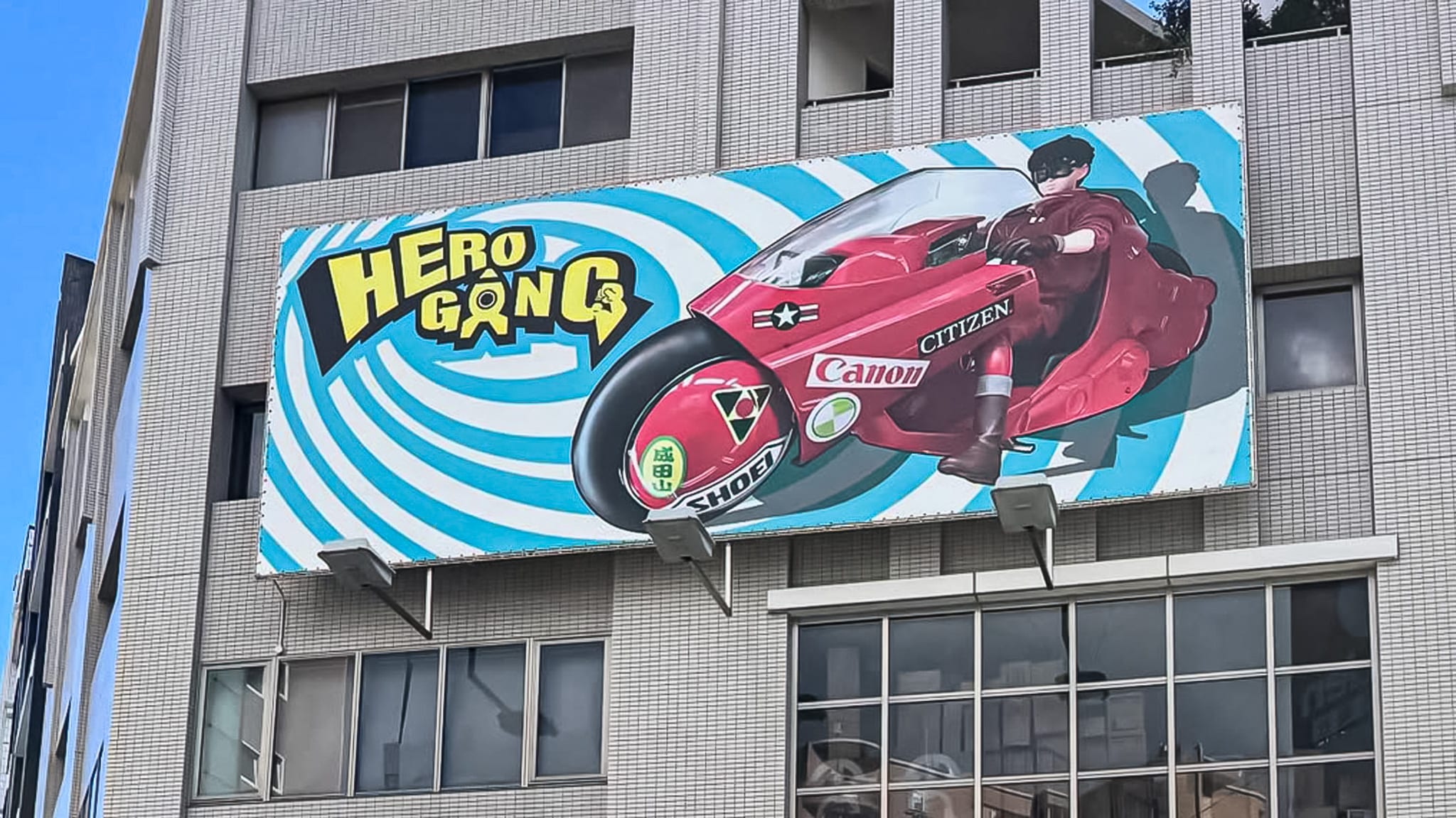 아키라의 시그니처 오토바이 프라모델이 전면에 걸려 있는 히어로 완구 연구소의 간판과 매장 정면